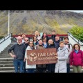 Zdjęcie przedstawia grupę 15 osób, która stoi przed budynkiem i trzyma tablicę z napisem FAB LAB Ísafjörður. 