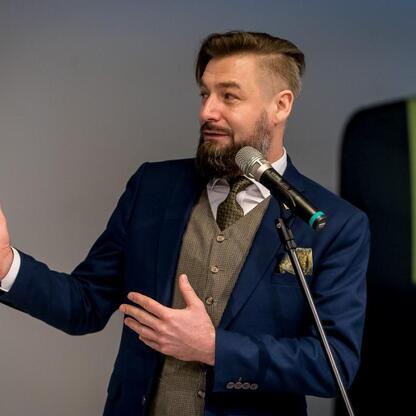 Mężczyzna w niebieskim garniturze prezentuje projekt wykorzystania wód pokopalnianych w Muzeum Śląskim w Katowicach. (wygenerowano przez AI)