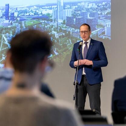 Mężczyzna w garniturze przemawia do publiczności w sali konferencyjnej, przedstawiając potencjał wykorzystania wód podziemnych w energetyce odnawialnej. (wygenerowano przez AI)