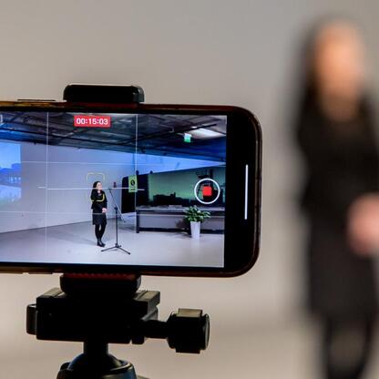 Smartfon montowany na statywie, nagrywający wideo z perspektywy osoby stojącej w nowoczesnym, przemysłowym pomieszczeniu z wysokimi sufitami i widocznymi beleami. (wygenerowano przez AI)
