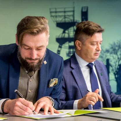Podpis: Dwa mężczyźni w strojach formalnych podpisują dokument, jednym z nich to dyrektor Muzeum Śląskiego w Katowicach. (wygenerowano przez AI)
