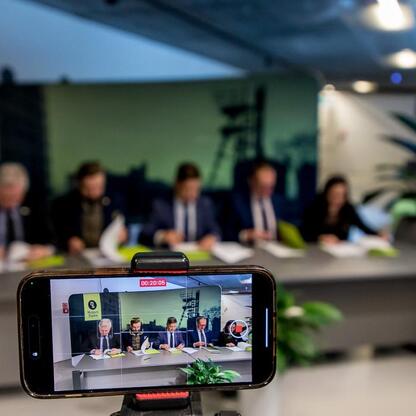 Zdjęcie przedstawia smartfon nagrywający wideo ze spotkania w Muzeum Śląskim w Katowicach, gdzie omawia się wykorzystanie wód pokopalnianych do produkcji energii odnawialnej. (wygenerowano przez AI)