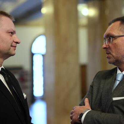 W dwóch mężczyznach w garniturach rozmawiają w nowoczesnym budynku, podkreślając współpracę międzynarodową. (wygenerowano przez AI)