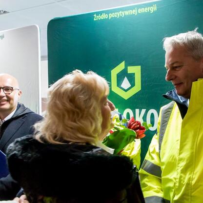 Grupa ludzi w żółtych kamizelkach zbierają się przed tablicą 