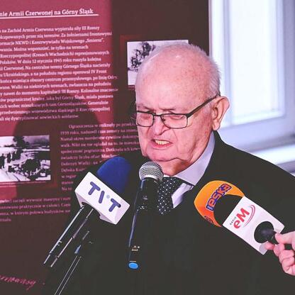 Stary mężczyzna przemawia do mikrofonu, uczestnicząc w uroczystości upamiętniającej 80. rocznicę Tragedii Górnośląskiej. (wygenerowano przez AI)