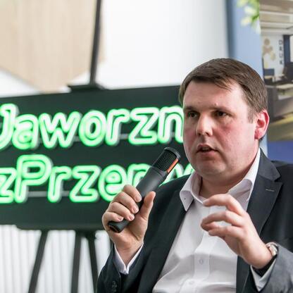 Mężczyzna w garniturze przemawia na konferencji w Jaworznie, temat: JOG, potencjał ekonomiczny. (wygenerowano przez AI)
