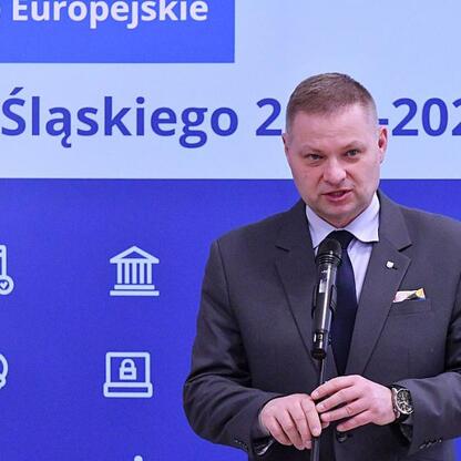Rafał Adamczyk, członek Zarządu Województwa Śląskiego, przemawia na podium o funduszach dla odnawialnych źródeł energii. (wygenerowano przez AI)