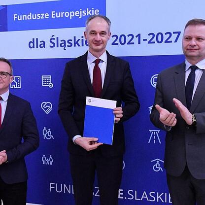 Trzech członków zarządu w formalnym stroju wręczają certyfikaty na tle 
