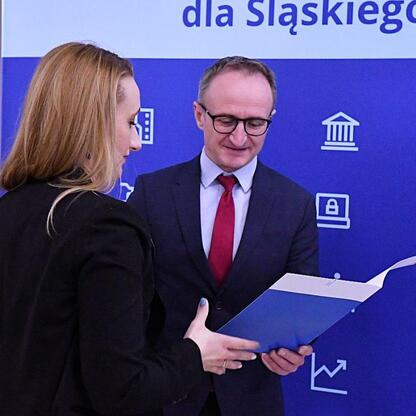 Wicemarszałek Grzegorz Boski i Marcin Ryś wręczają dokumenty przed sztandarem 