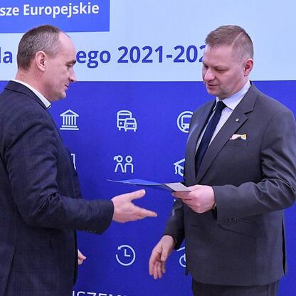 Rafał Adamczyk, członek Zarządu Województwa Śląskiego, wręcza dokument przedstawicielowi gminy w ramach ceremonii finansowania projektów odnawialnych źródeł energii. (wygenerowano przez AI)