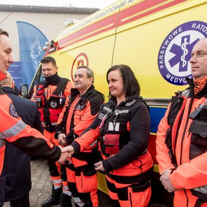 Nowoczesna karetkaEMS w mundurach pomarańczowych przed żółtym ambulansem, symbolizując nową flotę ratownictwa w Jaworznie. (wygenerowano przez AI)