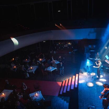 Jazzowa scena w klubie, muzyk gra na gitarze, publiczność siedzi przy stolikach z świecami. (wygenerowano przez AI)
