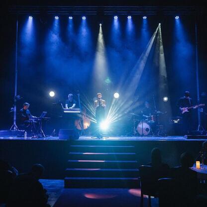 Live music performance at a cultural celebration in Śląsk, with dramatic blue lighting and attentive audience. (wygenerowano przez AI)