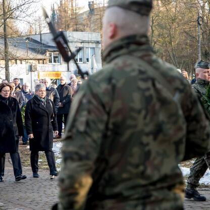 Słupski żołnierz w mundurze wojskowym przewozi wieniec z białymi kwiatami i czerwonymi makami, uczestnicząc w uroczystościach upamiętniających 80. rocznicę Tragedii Górnośląskiej. (wygenerowano przez AI)