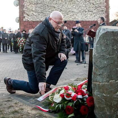 Na zdjęciu przedstawiono uroczystość upamiętniającą 80. rocznicę Tragedii Górnośląskiej. Uczestnik kłania się przy pomniku, podczas gdy inni obecni uczestniczą w ceremonii. (wygenerowano przez AI)