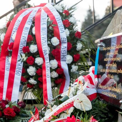 Wieniec z czerwonymi i białymi wstążkami i kwiatami ustawiony na pomniku w Bytomiu-Miechowicach, upamiętniającym ofiary Tragedii Górnośląskiej. (wygenerowano przez AI)