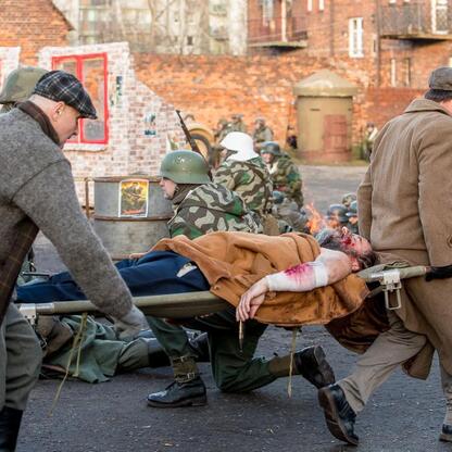 Rekonstrukcja zdarzeń z 1945 r. w Upper Silesia. Żołnierze transportują rannego, tło: zniszczone miasto. (wygenerowano przez AI)