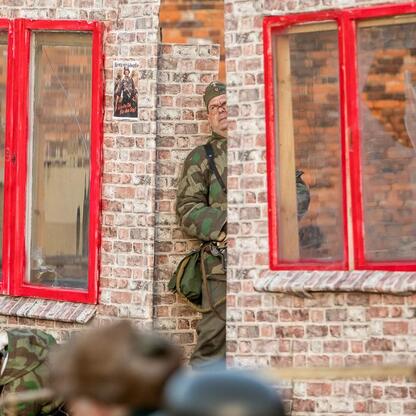 Soldier in military attire stands in a window of a brick building adorned with posters and graffiti, commemorating the Tragedy of Upper Silesia. (wygenerowano przez AI)