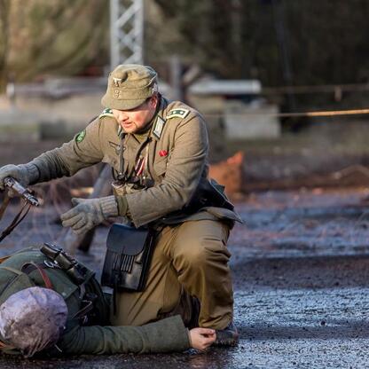 Rekonstrukcja z 1945 roku: żołnierz niemiecki pomaga rannemu przy pomniku Ofiar Tragedii Górnośląskiej. (wygenerowano przez AI)