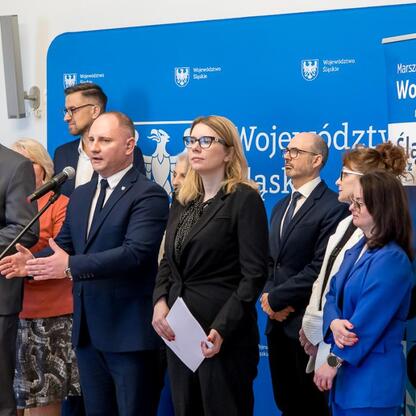 Zebrała się grupa osób w formalnym ubiorze przed logo i nazwą Województwa Śląskiego, podkreślając temat dostępności i inkluzji. (wygenerowano przez AI)
