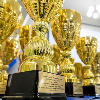 Złote trofea z tabliczkami ustawione w rzędzie, nagrody dla najlepszych szkół w Śląskim Związku Sportowym. (wygenerowano przez AI)