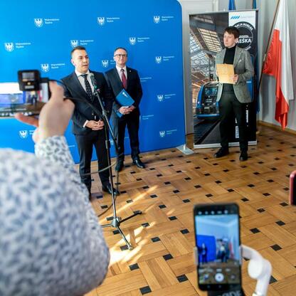 Wicemarszałek Województwa Śląskiego Grzegorz Boski i wiceprezes Kolei Śląskich Tomasz Niedziela prezentują nową ofertę dla dzieci i młodzieży podczas konferencji prasowej. (wygenerowano przez AI)