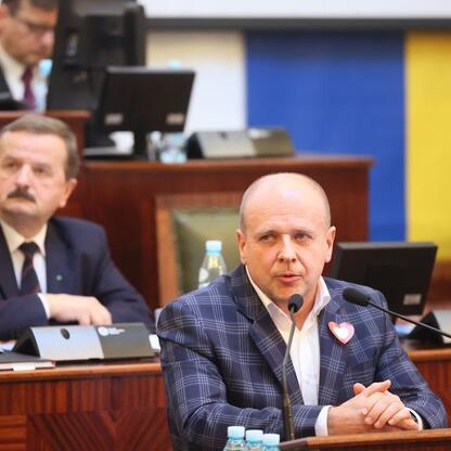 Siedzący przed mikrofonami i dokumentami w konferencyjnym pomieszczeniu reprezentują Sejmik Województwa Śląskiego, dyskutując nad finansami i infrastrukturą regionu. (wygenerowano przez AI)