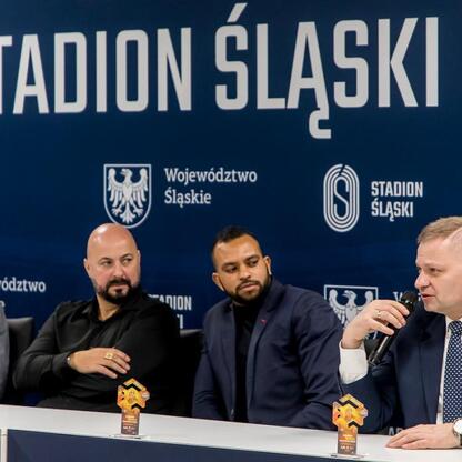 Konferencja prasowa przed meczem Ronaldinho Show na Stadionie Śląskim, gdzie Rafał Adamczyk omawia znaczenie wydarzenia. (wygenerowano przez AI)