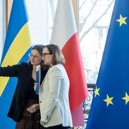 Dwie kobiety robią selfie przed flagami Ukrainy, Polski i Unii Europejskiej, w tle okno. (wygenerowano przez AI)