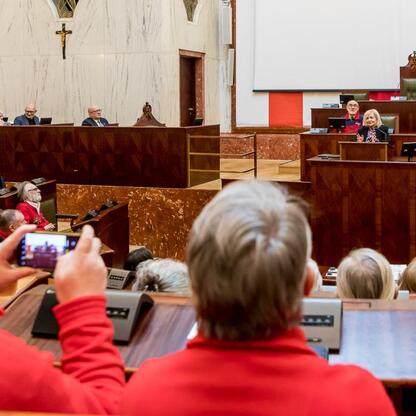 W Sali Sejmu Śląskiego obchodzony jest Międzynarodowy Dzień Przewodników Turystycznych. Uczestnicy, w większości w czerwonych kurtkach, siedzą w rzędach, słuchając przemówienia. (wygenerowano przez AI)