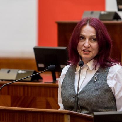 Kobieta z fioletowymi włosami przemawia na podium w Śląskim Sejmie, uczestnicząc w obchodach Międzynarodowego Dnia Przewodników Turystycznych. (wygenerowano przez AI)