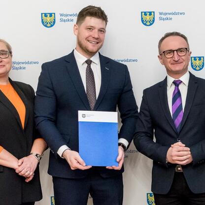 Wicemarszałek Grzegorz Boski prezentuje dokument na tle logo Województwa Śląskiego. (wygenerowano przez AI)