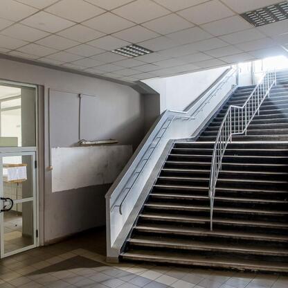 Wnętrze budynku w trakcie przebudowy, oświetlone przez duże okno, z widoczną schodami prowadzącymi w górę. (wygenerowano przez AI)