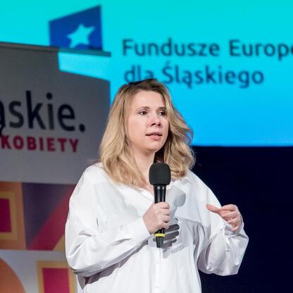 Na konferencji o równości płci i współpracy między pokoleniami, kobieta wita publiczność. (wygenerowano przez AI)