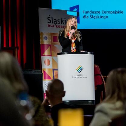 Joanna Bojczuk, członek Zarządu Województwa Śląskiego, przemawia na konferencji o funduszach europejskich dla kobiet. (wygenerowano przez AI)