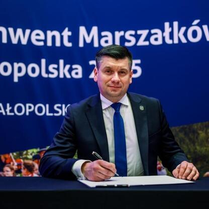 Mężczyzna w garniturze podpisuje dokument na konwencie Marszałków w Małopolsce 2025. (wygenerowano przez AI)