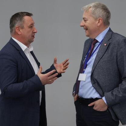 Dwa mężczyźni w strojach formalnych prowadzą rozmowę, podkreślając znaczenie dyskusji o polityce Zielonego Ładu w kontekście gospodarki śląskiej. (wygenerowano przez AI)