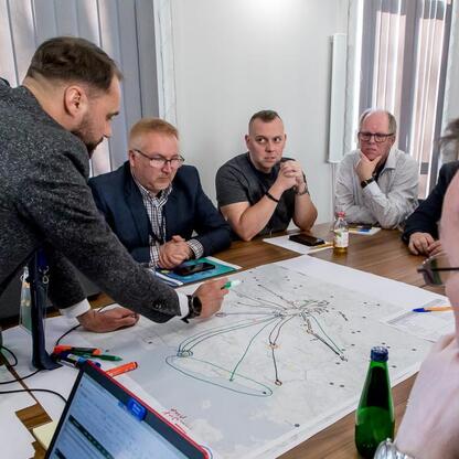 Grupa mężczyzn dyskutuje nad mapą i laptopem, planując rozwój sieci kolejowej województwa śląskiego. (wygenerowano przez AI)