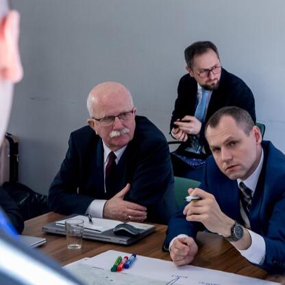 Grupa mężczyzn w formalnym ubiorze uczestniczy w warsztatach dotyczących Zintegrowanej Sieci Kolejowej w Urzędzie Marszałkowskim Województwa Śląskiego. (wygenerowano przez AI)
