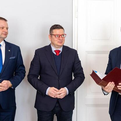 Trzech mężczyzn w formalnym stroju biznesowym stoi przed drzwiami biurowymi, omawiając plany pracy Wojewódzkiej Rady Rynku Pracy. (wygenerowano przez AI)