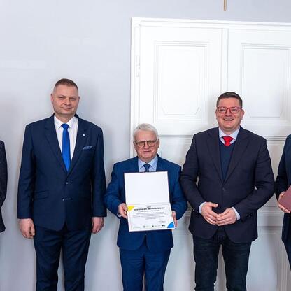 Grupa sześciu mężczyzn w strojach formalnych uczestniczy w ceremonii nagradzającej lub uroczystości związanych z Wojewódzką Radą Rynku Pracy. (wygenerowano przez AI)