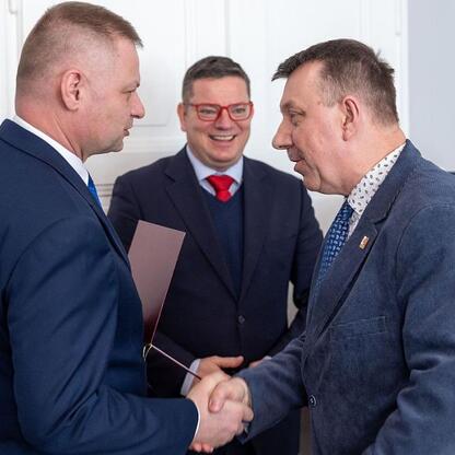 Rafał Adamczyk, członek zarządu Województwa Śląskiego, podczas spotkania Wojewódzkiej Rady Rynku Pracy, gdzie dwaj mężczyźni w garniturach składają sobie ręce, symbolizując formalne porozumienie. (wygenerowano przez AI)