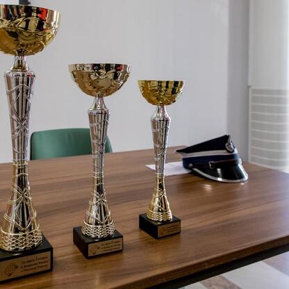 Trzy trofea na drewnianym stole, nagrody dla zwycięzców konkursu wiedzy o pierwszej pomocy województwa śląskiego. (wygenerowano przez AI)