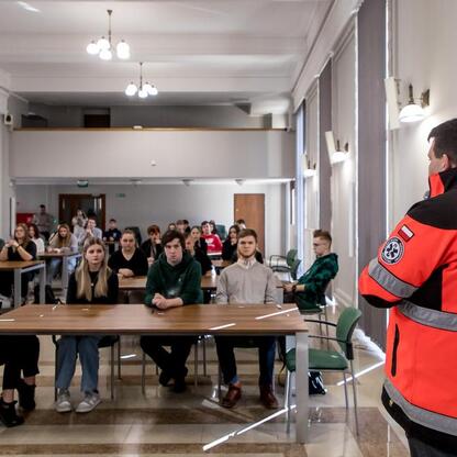 Na zdjęciu: Uczestnicy konkursu wiedzy o pierwszej pomocy podczas finału wojewódzkiego, prowadzony przez instruktora w mundurze. (wygenerowano przez AI)