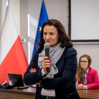 Kobieta w czarnym płaszczu przemawia do publiczności na konferencji w Śląsku. (wygenerowano przez AI)