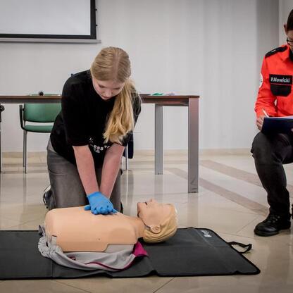 Uczestnik konkursu demonstruje CPR na manekinie pod okiem sędziego P.Nowickiego. (wygenerowano przez AI)