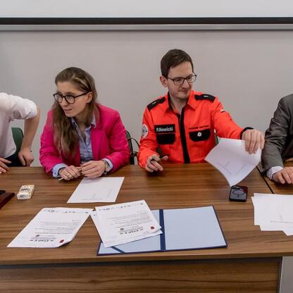 Wojewódzka konkurs wiedzy o pierwszej pomocy, uczestnicy w konferencyjnym pomieszczeniu, dyskusja o wynikach. (wygenerowano przez AI)