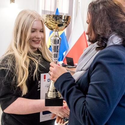 Zakończenie konkursu wiedzy o pierwszej pomocy województwa śląskiego. Uczestnicy wymieniają trofeum, symbolizujące ich sukces. (wygenerowano przez AI)