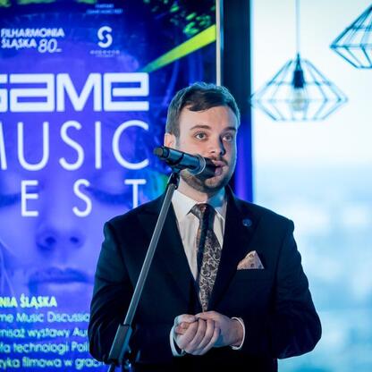 Na festiwalu Game Music Festival mąż w garniturze przemawia do mikrofonu. (wygenerowano przez AI)