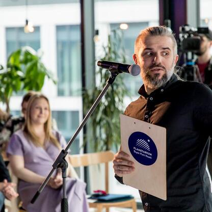 Mężczyzna przemawia na podium podczas konferencji prasowej Game Music Fest, festiwalu muzyki z gier komputerowych. (wygenerowano przez AI)